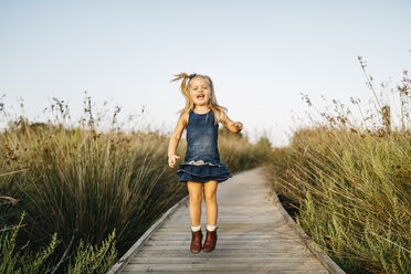 Happy little girl jumping on boardwalk in nature - JRFF00867