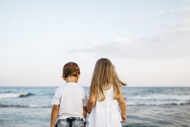 Back view of little boy and girl standing side by side in front of the sea - JRFF00884