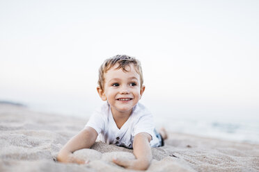 Portrait of happy little boy lying on the beach - JRFF00896