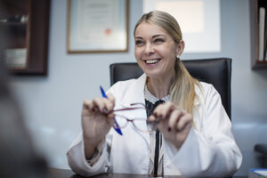 Female optometrist talking to patient, holding spectacles - ZEF10576