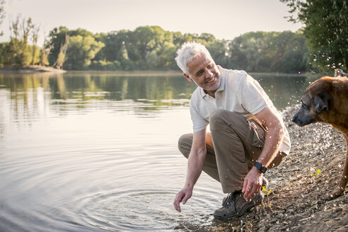 Senior man playing with dog at a lake - ONF01030