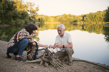 Senior couple lighting a campfire at a lake in the evening - ONF01044