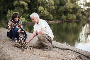 Senior couple lighting a campfire at a lake in the evening - ONF01045