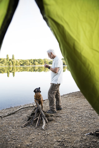 Älterer Mann mit Hund beim Zelten an einem See, lizenzfreies Stockfoto