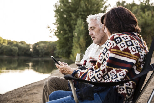 Älteres Paar mit Wein an einem See sitzend mit Tablet - ONF01083
