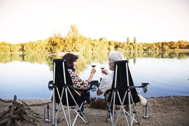 Senior couple clinking wine glasses at a lake in the evening - ONF01084
