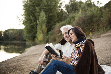 Happy senior couple with wine and book at a lake - ONF01088