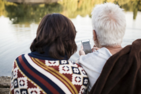 Älteres Paar mit Handy an einem See, lizenzfreies Stockfoto