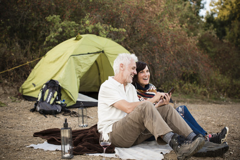 Glückliches älteres Paar mit Handy in einem Zelt, lizenzfreies Stockfoto