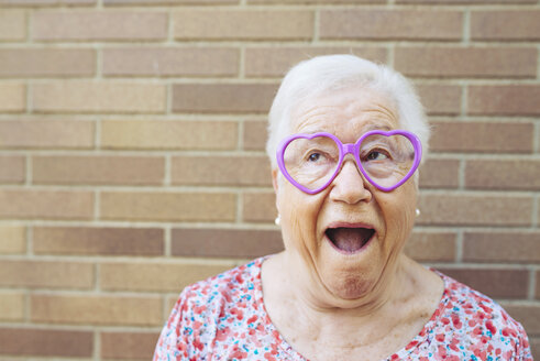 Portrait of senior woman wearing heart-shaped glasses pulling funny faces - GEMF01120