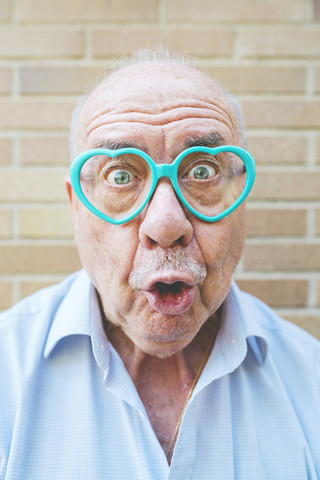 Porträt eines älteren Mannes mit herzförmiger Brille, der lustige Grimassen zieht, lizenzfreies Stockfoto