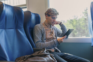 Junger Mann sitzt in einem Zug und schaut auf ein Tablet - FMOF00133