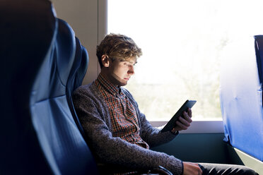 Young man sitting in a train looking at tablet - FMOF00135