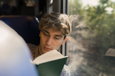 Young man reading book in a train - FMOF00136