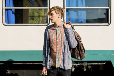 Young man with leather bag standing in front of a train - FMOF00139