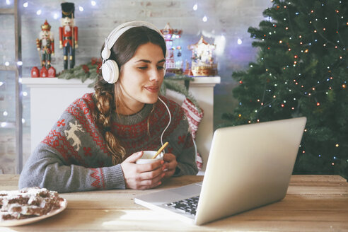 Frau mit einer Tasse Kaffee, Laptop und Kopfhörern zur Weihnachtszeit - RTBF00430