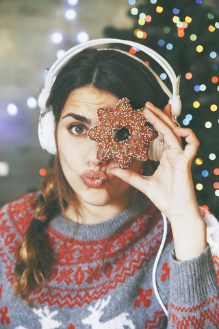 Frau mit Kopfhörern schaut durch einen Weihnachtskeks, lizenzfreies Stockfoto