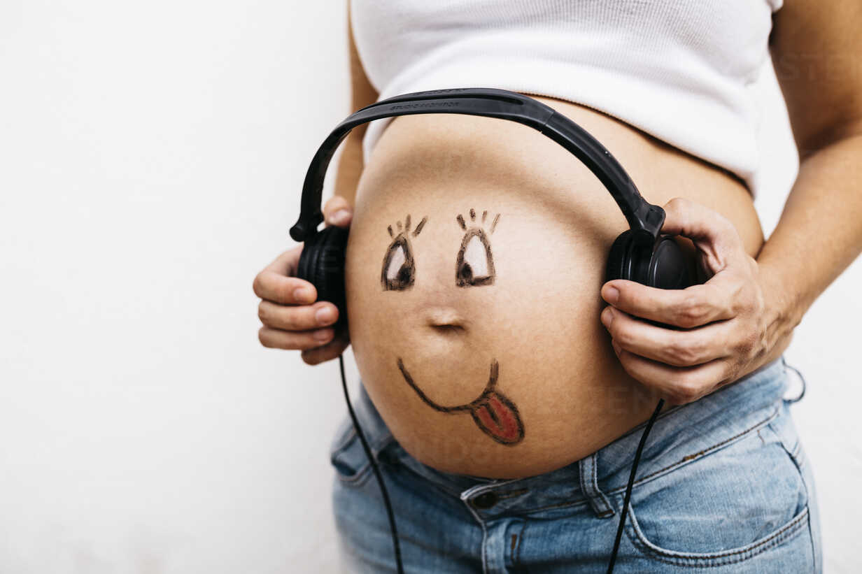 Pregnant woman putting headphones on her belly Stock Photo