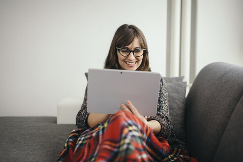 Young woman covered with blanket relaxing on the couch with her tablet - LCUF00043