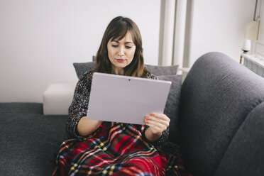 Junge Frau mit Decke zugedeckt entspannt auf der Couch mit ihrem Tablet - LCUF00044