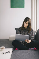 Young woman sitting on the couch using her tablet - LCUF00045