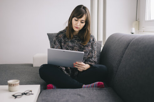 Young woman sitting on the couch using her tablet - LCUF00046