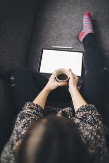 Draufsicht auf eine Frau, die mit einem Tablet und einer Tasse Kaffee auf der Couch sitzt - LCUF00048