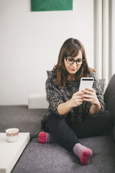 Young woman relaxing on the couch looking at her smartphone - LCUF00052