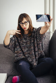 Junge Frau entspannt sich auf der Couch und macht ein Selfie mit ihrem Smartphone - LCUF00053