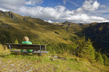 Österreich, Kärnten, Drautal, Frau sitzt auf Bank in Berglandschaft - GFF00790