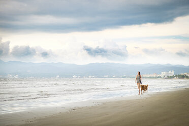 Mexico, Nayarit, Young woman walking Golden Retriever dog at the beach - ABAF02076