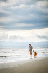 Mexico, Nayarit, Young woman walking Golden Retriever dog at the beach - ABAF02077