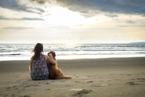 Mexico, Nayarit, Back view of young woman sitting next to her dog at the beach - ABAF02078