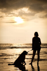 Mexico, Nayarit, silhouette of young woman with her dog on a leash at a beach at sunset - ABAF02079