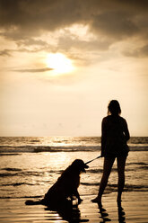 Mexiko, Nayarit, Silhouette einer jungen Frau mit ihrem Hund an der Leine an einem Strand bei Sonnenuntergang - ABAF02079