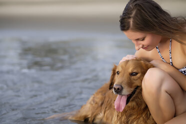 Nahaufnahme einer jungen Frau im Bikini, die ihren Golden Retriever Hund am Strand streichelt - ABAF02080