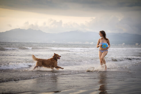 Mexiko, Nayarit, Junge Frau im Bikini spielt Frisbee mit ihrem Golden Retriever Hund am Strand - ABAF02082
