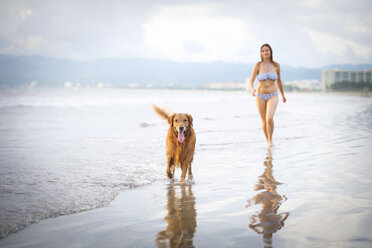 Mexiko, Nayarit, Junge Frau geht mit ihrem Golden Retriever Hund am Strand spazieren - ABAF02083