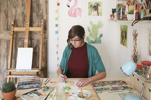 Frau malt ein Aquarell einer Ananas am Schreibtisch in ihrem Atelier - RTBF00433