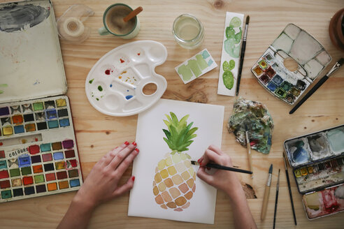 Eine Frau malt mit der Hand ein Aquarell einer Ananas auf dem Schreibtisch in ihrem Atelier - RTBF00434