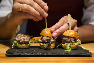 Man sticking a skewer in a mini burger of red tuna - ABZF01367