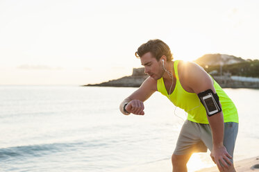 Spanien, Mallorca, Jogger am Strand mit Kopfhörern, Blick auf Smartwatch - DIGF01363