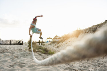 Spanien, Mallorca, Jogger springt morgens am Strand über ein Seil - DIGF01379