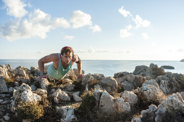 Spanien, Mallorca, Sportler steht morgens an der Felsenküste, Liegestütz - DIGF01392