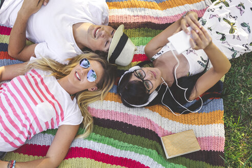 Junge Frau mit Freunden auf einer Decke liegend und Musik hörend - DAPF00365