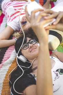Junge Frau mit Freunden auf einer Decke liegend und Musik hörend - DAPF00367