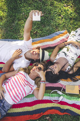 Playful friends lying on blanket in park taking a selfie - DAPF00368