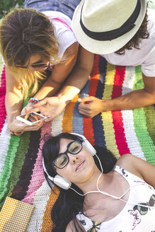 Junge Frau mit Freunden auf einer Decke liegend und Musik hörend - DAPF00369