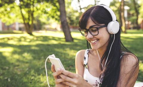 Glückliche junge Frau im Park beim Musikhören, lizenzfreies Stockfoto