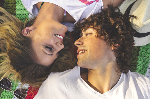 Lächelndes junges Paar, das auf einer Decke liegt und sich gegenseitig ansieht - DAPF00375